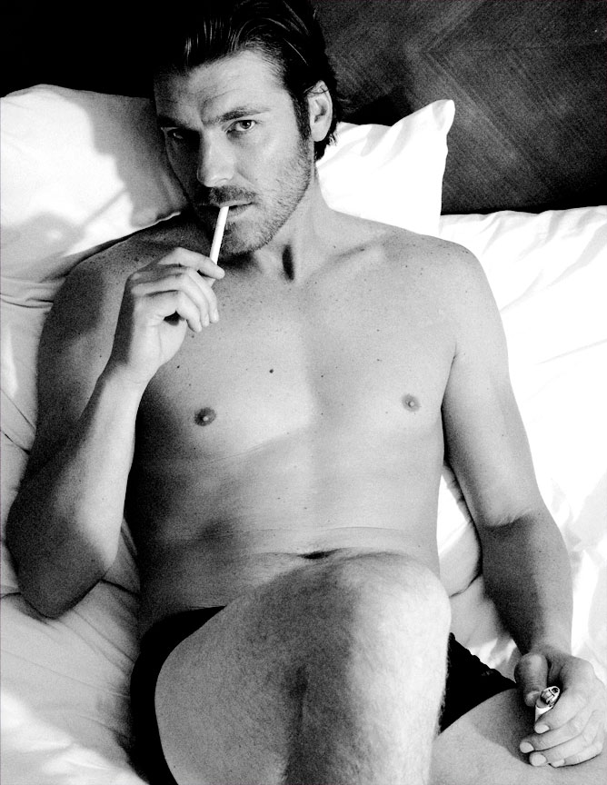 Topless guy smoking a cigerette in bed